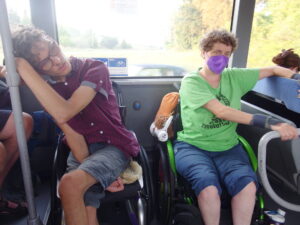 zwei Rollstuhlfahrende in einem Bus, sehen sehr müde aus