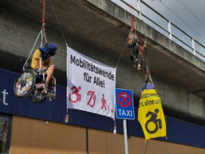 Nahaufnahme Banner Aktion, 2 Rollstuhlfahrer*innen und ein Banner 'Mobilitätswende für alle' und ein Banner 'Mobilitätswende nicht ohne uns'
