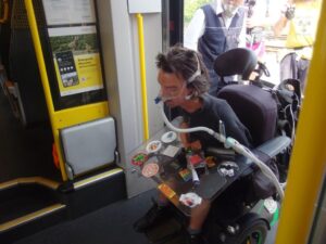 Ein Mensch in einem schwerem Rollstuhl der kuenstlich beatmet wird steigt in den Zug.