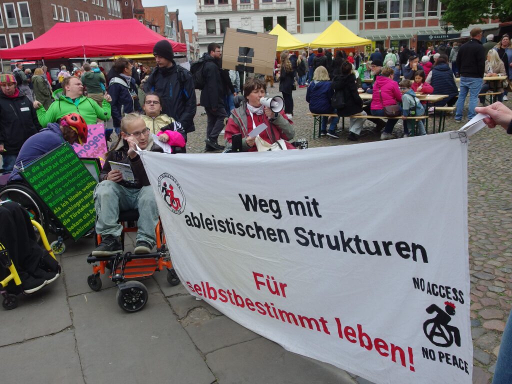 Demonstrierende mit Banner ein Kind im Rollstuhl hält ein Banner: "Weg mit ableitischen Strukturen. Für selbstbestimmt leben!